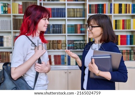 Female teacher talking to teenage student girl, inside library
