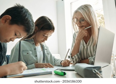 Female Teacher Or Tutor Diverse Kids Children Asian Boy And Latin Girl Students With Homework Learning Sitting At Desk In Classroom. After School Education And Day Care Studies Concept.