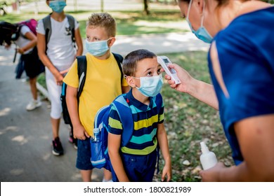 Female teacher using thermometer temperature screening on children  for fever against the spread virus while student is coming back to school. - Powered by Shutterstock