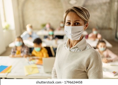 Female teacher wearing a face mask while teaching children at elementary school and looking at camera.  - Powered by Shutterstock