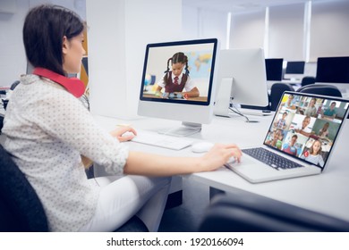 Female Teacher Wearing Headphones Having A Video Call With Multiple Students At School On Laptop And Computer. Distance Learning Online Education Concept