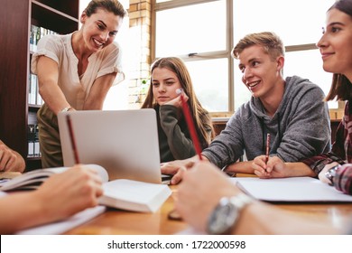 Female teacher working with college students in library. Group of students studying in school library with a teacher helping them.