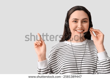 Female technical support agent in headset pointing at something on grey background