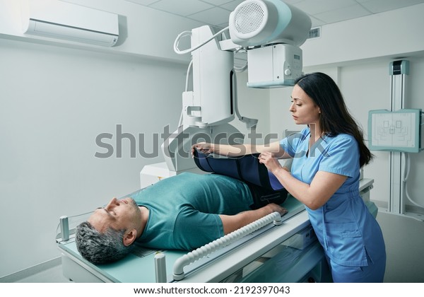Female\
technician preparing patient for body X-ray in radiographic imaging\
room, putting for him radiation protection\
apron
