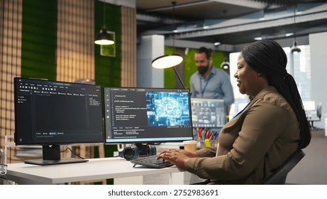 Female technician using computer to write code, developing machine learning APIs. African american woman troubleshooting software errors and faults using artificial intelligence, camera A