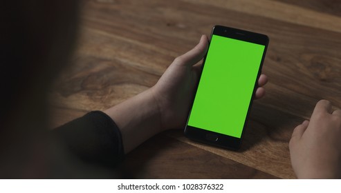 female teen girl holding smartphone with green screen sitting at the table - Powered by Shutterstock