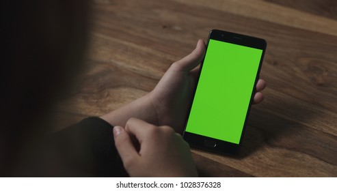 female teen girl holding smartphone with green screen sitting at the table - Powered by Shutterstock