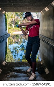 Female Teen Softball Player Relaxing In Backlit Tunnel With Bat Swinging Across Strike Zone.