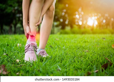 Female teenager hand touching painful twisted or ankle sprain,feel ache,ankle injury after exercise in green nature,asian child girl have leg pain,problem,accident while running,playing in grass park