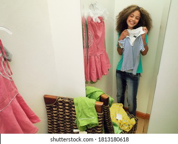 A Female Teenager Smiling At The Mirror As She Tries Out New Clothes In The Trial Room.