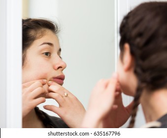 Female teenager squeezing acne spots alone at home