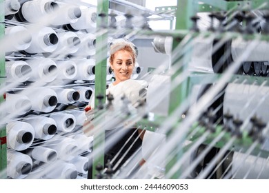 Female textile factory worker changing thread spool on industrial knitting machine. - Powered by Shutterstock