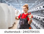 Female textile factory worker with thread spools holding thumbs up.