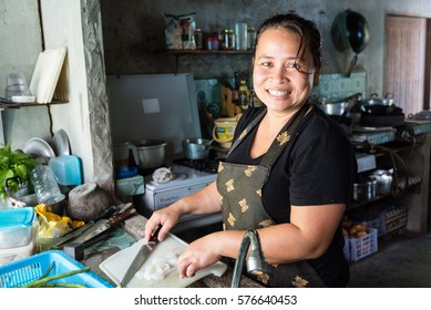 Female Thai chef smiling at camera, cutting meat for meal preparation