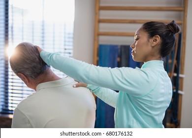 Female Therapist Examining Neck Of Senior Male Patient At Hospital Ward