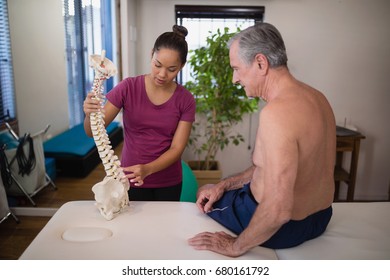 Female therapist explaining shirtless senior male patient with artificial spine at hospital ward - Powered by Shutterstock