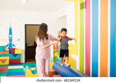 Female Therapist Helping A Kid To Maintain Balance While Walking On A Beam In A Therapy Center