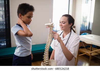 Female therapist pointing at artificial spine while explaining to boy in hospital ward - Powered by Shutterstock