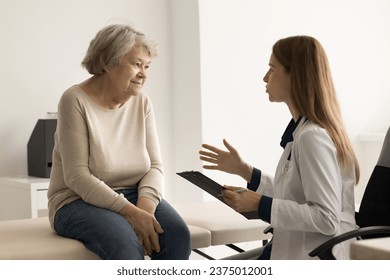 Female therapist in uniform talking to elderly retiree woman, asks about illness, gives professional medical help. Senior patient tells about health complaints at visit in clinic. Check-up, medicine - Powered by Shutterstock