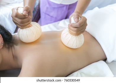 Female therapist using steamed Thai Herbal Compresses to relieve pain and inflammation for young Asian client , Thai traditional massage in Spa salon