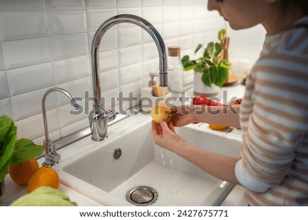 Female thoroughly washing fresh yellow apple in tap water to clean from food wax covering. Nutritional supplements prolonging fruit storage life. Oranges, banana lying on table. Healthy useful food