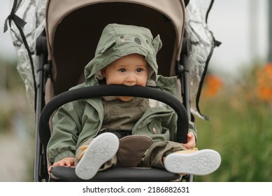 A female toddler is eating the safety bumper bar of her stroller on a cloudy day. A young girl in a baby carriage in a village green. - Shutterstock ID 2186882631