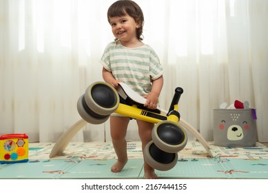 Female Toddler Holding Her Yellow Tricycle While Is Laughing And Running To The Camera. Playful And Happiness Concept.