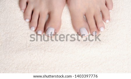 Female toes with white pedicure on ivory terry towel, close up. Woman bare feet. Spa, treatment, beauty, massage and care concept
