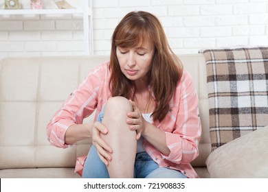 Female Touching Her Sore Knee. Woman At Home Background. Copy Space And Mock Up.