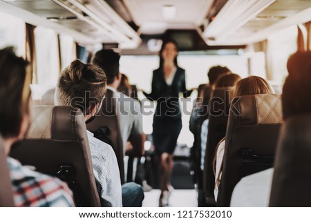 Female Tour Service Employee at Work on Tour Bus. Young Smiling Woman Standing between Passenger Seats of Touristic Bus. Traveling, Tourism and People Concept. People on Trip. Summer Vacation