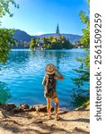 Female tourist with backpack and hat admiring the assumption of mary pilgrimage church on lake bled island, a famous travel destination in the julian alps