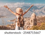 Female tourist with backpack raising arms, enjoying panoramic view of Kotor bay and old town, Montenegro