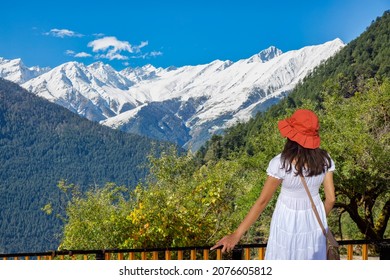 Female tourist enjoying the scenic landscape view and snow peaks of the Kailash Himalaya range from a hotel balcony at Kalpa Himachal Pradesh India