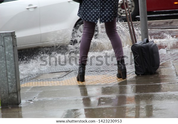 Female Tourist Getting Splashed\
by a Car Driving Into a Roadside Puddle on a Rainy Day in\
Edinburgh