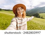 Female tourist is making a selfie in the middle of hills surrounded by green nature. Technology, travel, blogging concept.