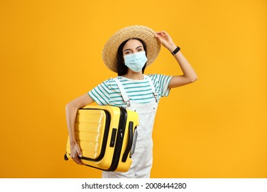 Female tourist in medical mask with suitcase on yellow background. Travelling during coronavirus pandemic - Powered by Shutterstock