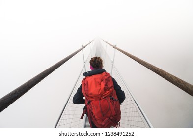 Female tourist walking across a suspension bridge into heavy fog