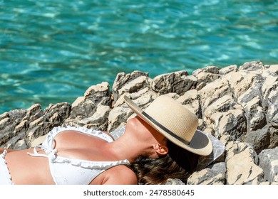 Female tourist wearing sun hat while sunbathing on rocky beach. Red skin and sunburns on chest from not using enough sunscreen. - Powered by Shutterstock