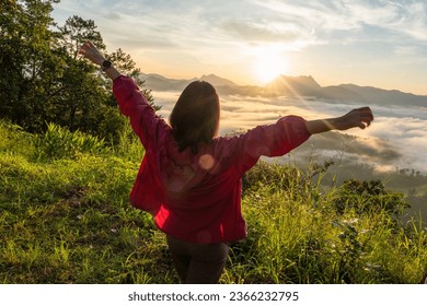 Female tourists carry backpacks, travel, hike, watch the mist as the sun rises to the top of the mountain, and relax, stretching their arms, feeling free in the morning, weekend holidays.