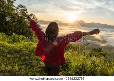 Female tourists carry backpacks, travel, hike, watch the mist as the sun rises to the top of the mountain, and relax, stretching their arms, feeling free in the morning, weekend holidays.