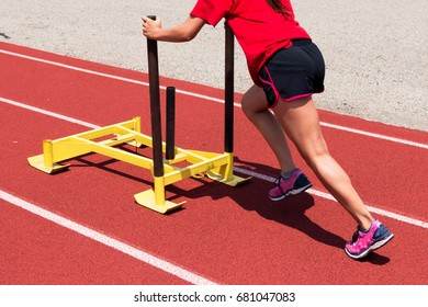 A female track and field athlete pushing a yellow sled down the track at practice for strength training
