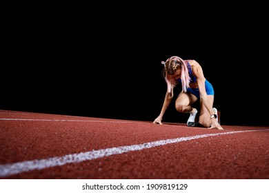 Female track runner on the starting block against black background