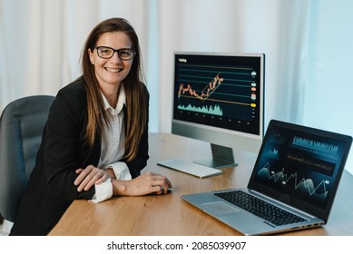 Female Trader At Table With Laptop And Computer Monitor