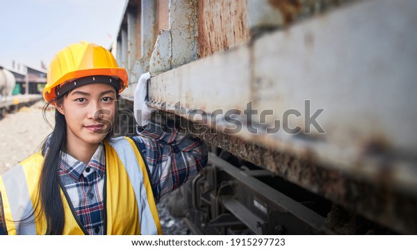 A female train maintenance engineer stands\
outdoors near a freight train waiting for a safety inspection,\
evaluation, and maintenance.