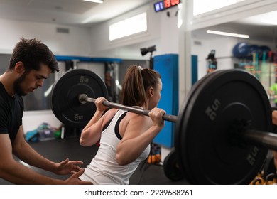 A female trainee lifting weights while being watched by her coach