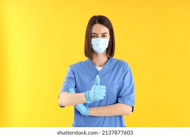 Female Trainee Nurse In Gloves And Mask On Yellow Background