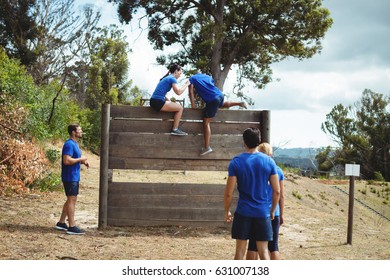 Female trainer assisting fit man to climb over wooden wall during obstacle course in bootcamp - Powered by Shutterstock