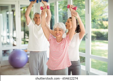 Female trainer assisting senior couple in performing exercise at home - Powered by Shutterstock