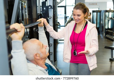 female trainer assisting senior man in lifting weight at gym