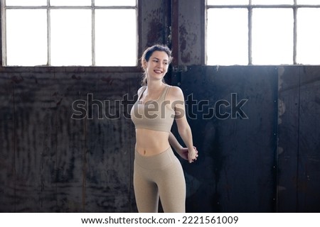 female trainer standing and stretching her arms behind her back in sportswear indoors, woman after exercise relax with cooldown at gym